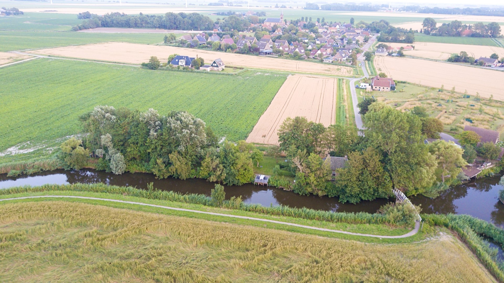 Het dorp achter de akkers, met het water en het huis tussen de bomen op de voorgrond