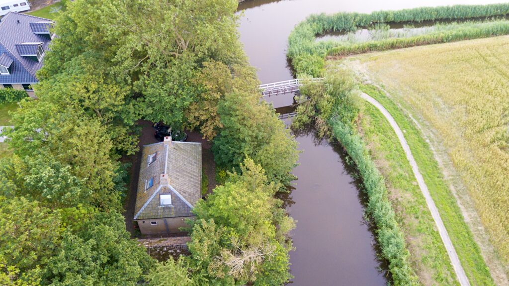Het vissershuis van bovenaf, met de brug en het pad langs het water